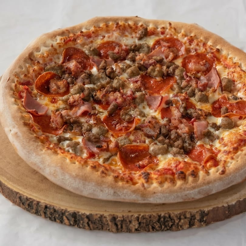 A whole meat lover's pizza with pepperoni, sausage, and ham on a wooden board.